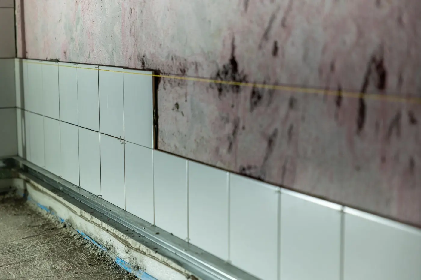 Tegelwand in aanbouw met lichtblauwe tegels en een waterpaslijn